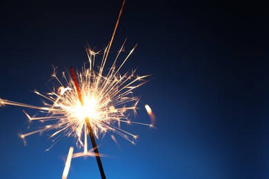 Photo of Bright burning sparkler on dark blue background, closeup. Space for text