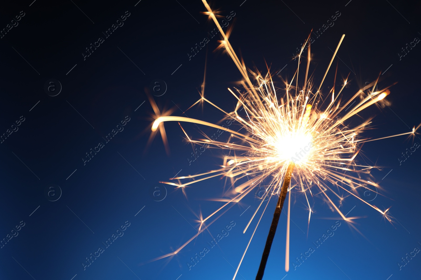 Photo of Bright burning sparkler on dark blue background, closeup. Space for text