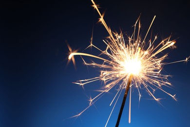 Photo of Bright burning sparkler on dark blue background, closeup. Space for text