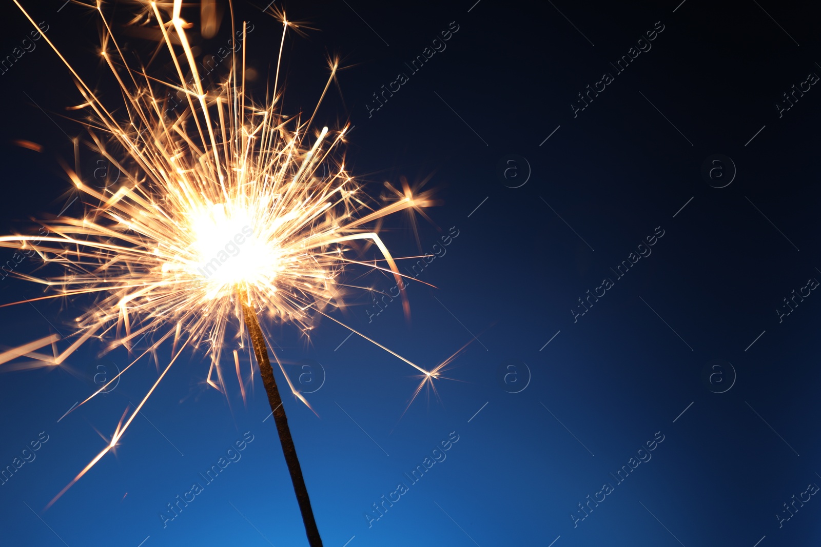 Photo of Bright burning sparkler on dark blue background, closeup. Space for text