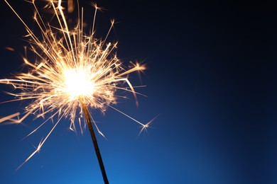 Photo of Bright burning sparkler on dark blue background, closeup. Space for text