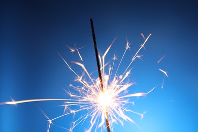 Photo of Bright burning sparkler on blue background, closeup