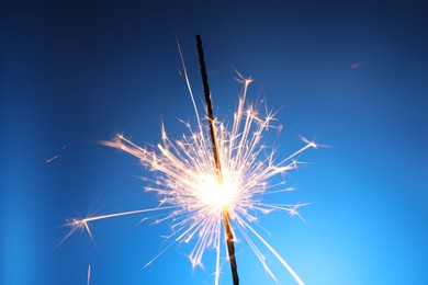 Photo of Bright burning sparkler on blue background, closeup