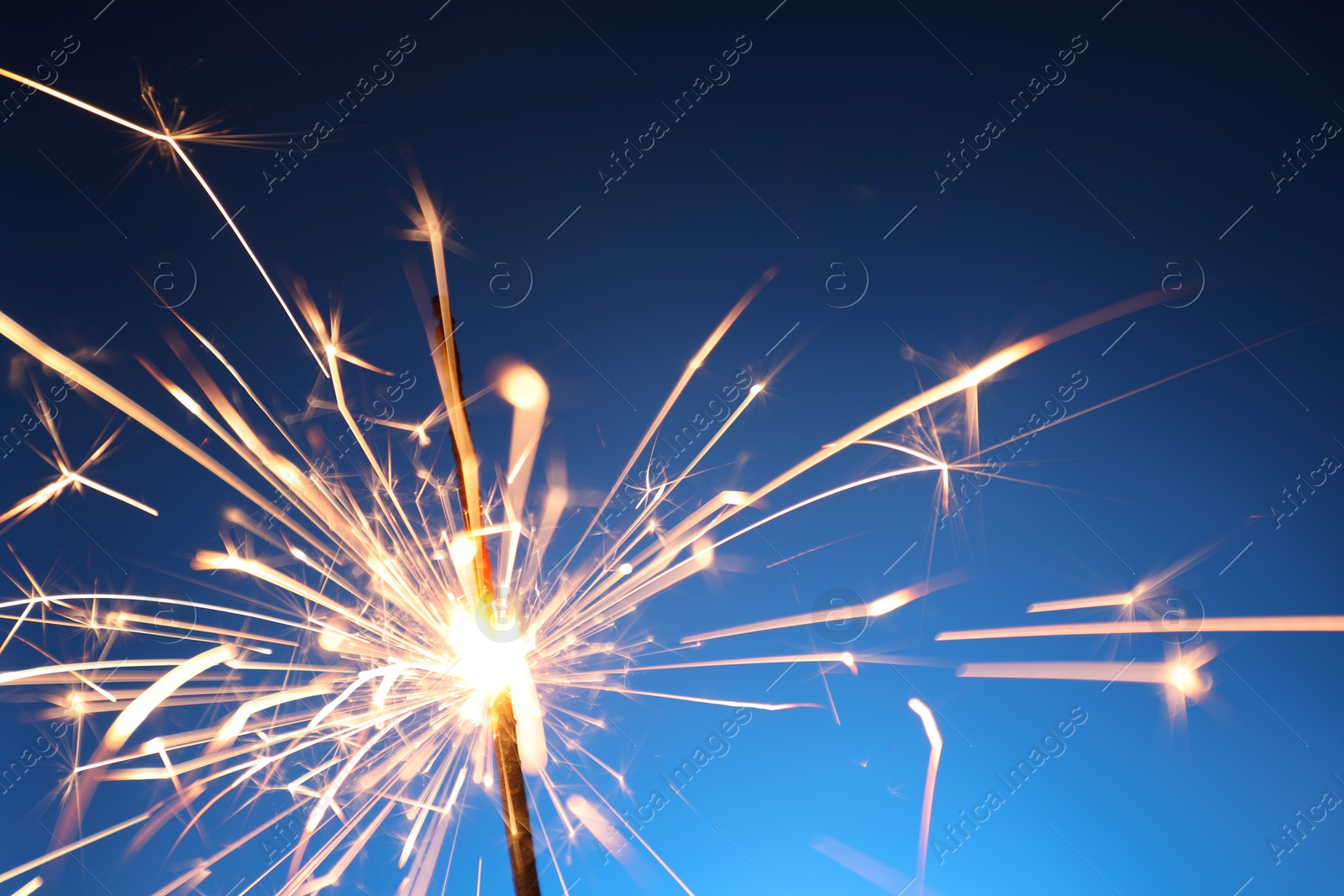 Photo of Bright burning sparkler on blue background, closeup