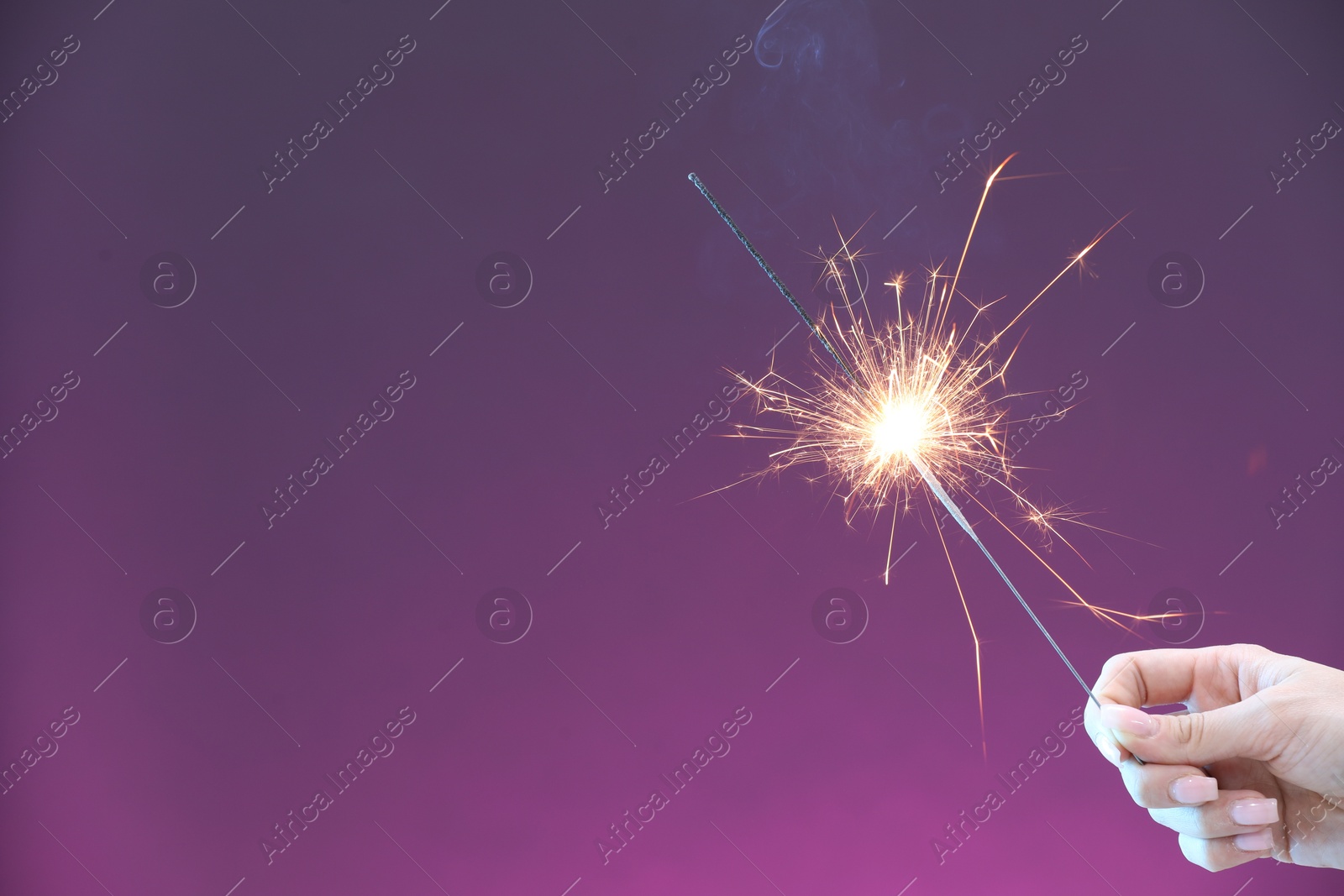 Photo of Woman with burning sparkler on violet background, closeup. Space for text