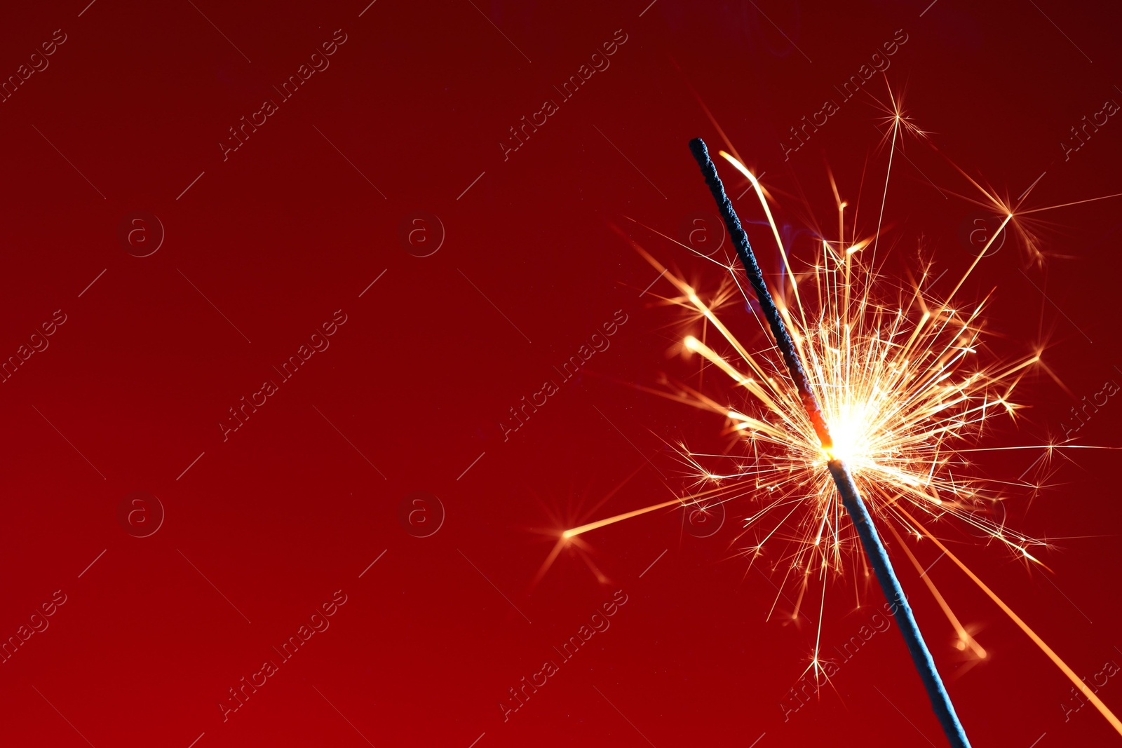 Photo of Bright burning sparkler on red background, closeup. Space for text