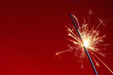 Photo of Bright burning sparkler on red background, closeup. Space for text