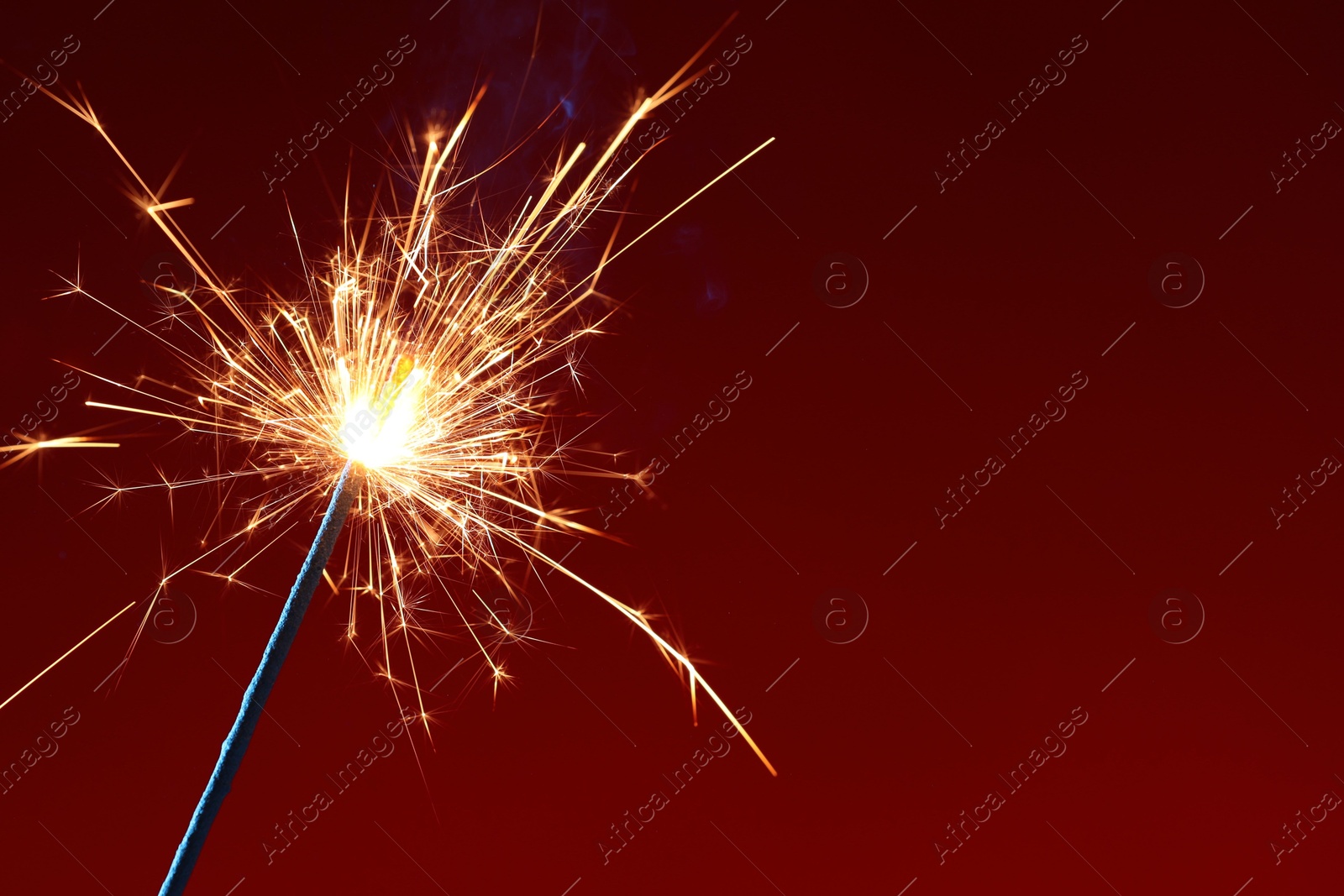 Photo of Bright burning sparkler on dark red background, closeup. Space for text