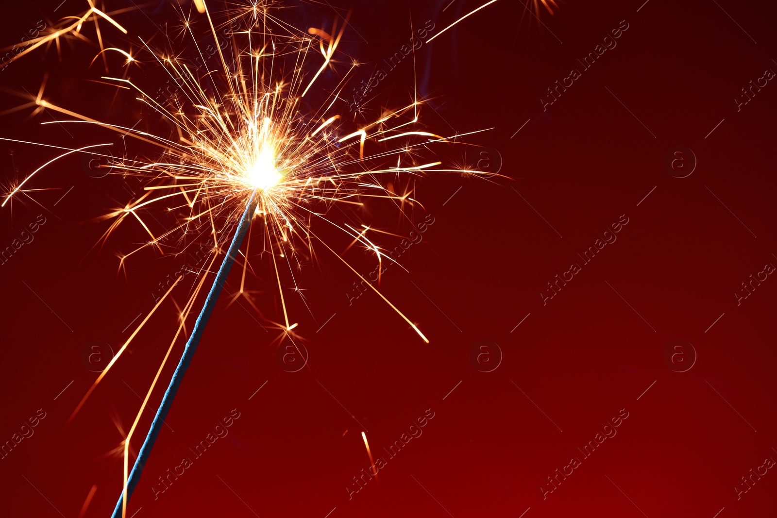 Photo of Bright burning sparkler on dark red background, closeup. Space for text