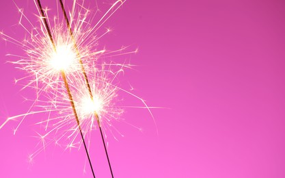 Photo of Bright burning sparklers on pink background, closeup. Space for text