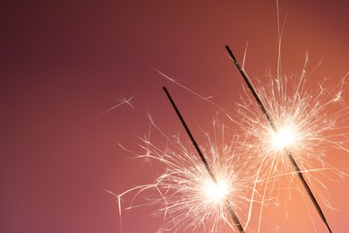 Photo of Bright burning sparklers on color background, closeup. Space for text