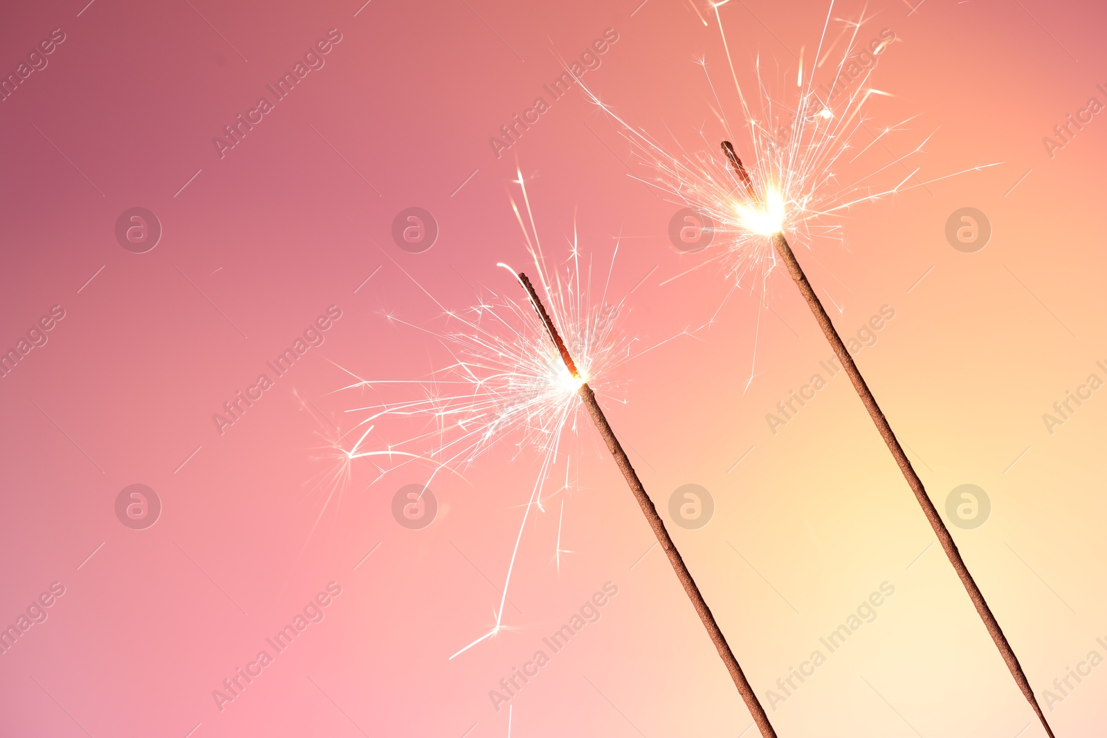 Photo of Bright burning sparklers on color gradient background, closeup. Space for text