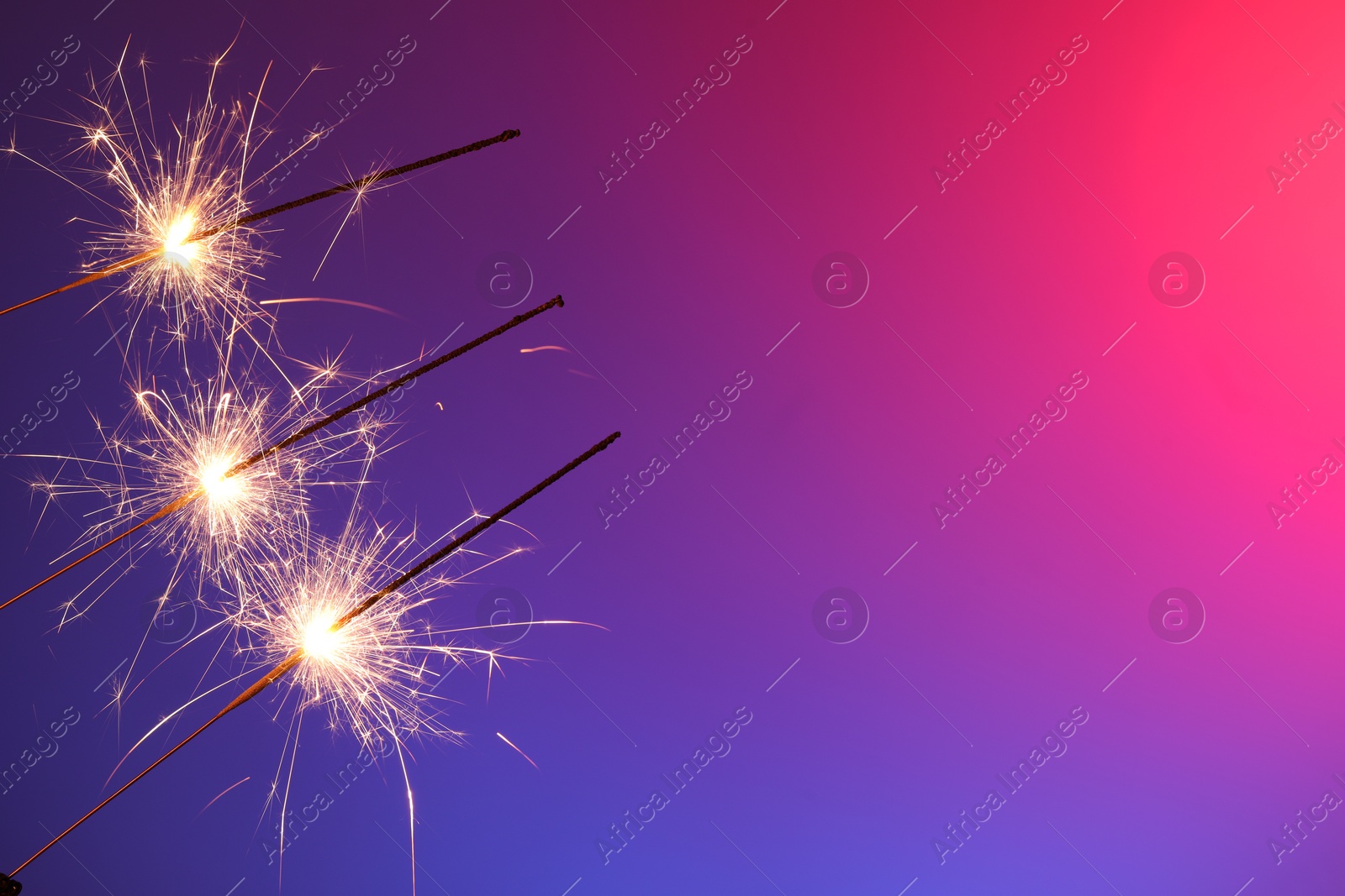 Photo of Bright burning sparklers on color gradient background, closeup. Space for text