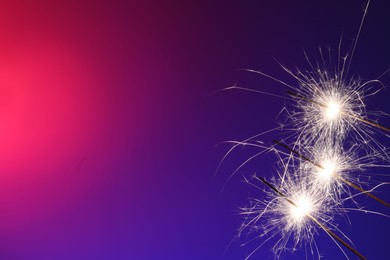 Photo of Bright burning sparklers on color gradient background, closeup. Space for text