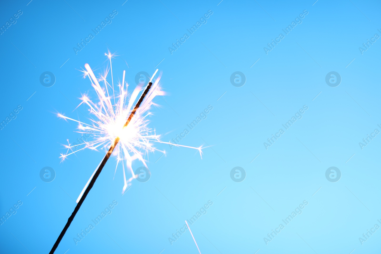 Photo of Bright burning sparkler on light blue background, closeup. Space for text