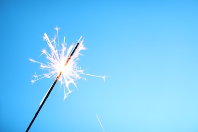 Photo of Bright burning sparkler on light blue background, closeup. Space for text