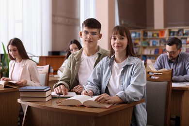 Portrait of young couple with books at desk in public library