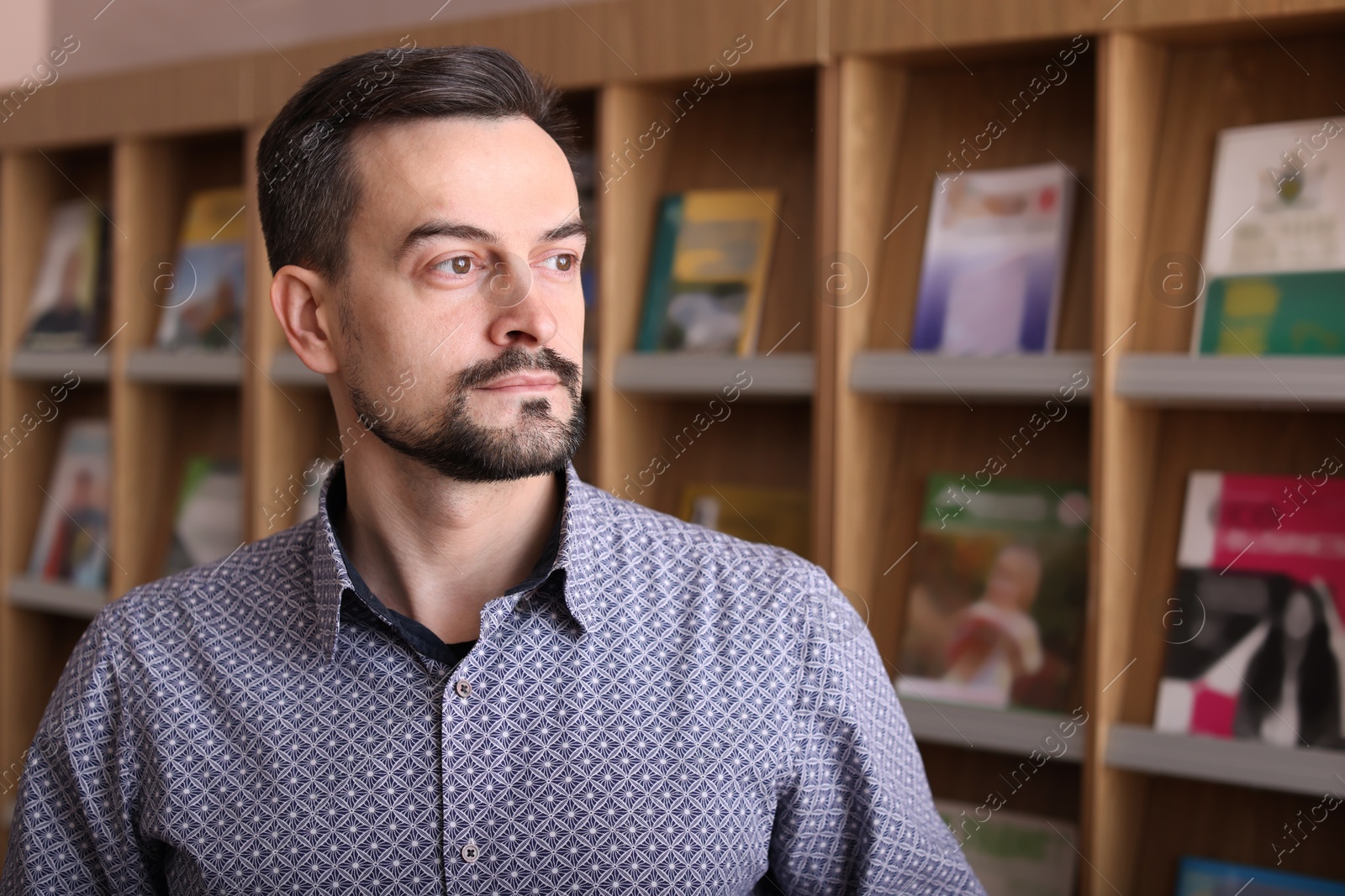 Photo of Portrait of handsome man near bookshelf in library. Space for text