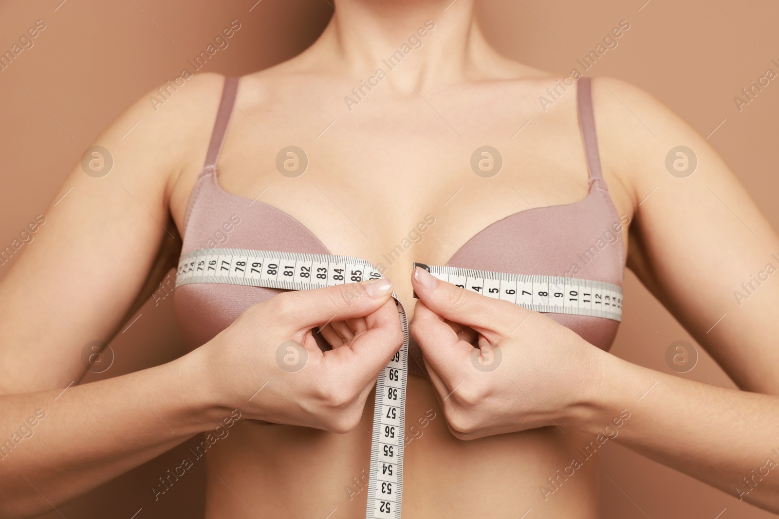 Photo of Woman in beautiful bra measuring breast circumference on beige background, closeup