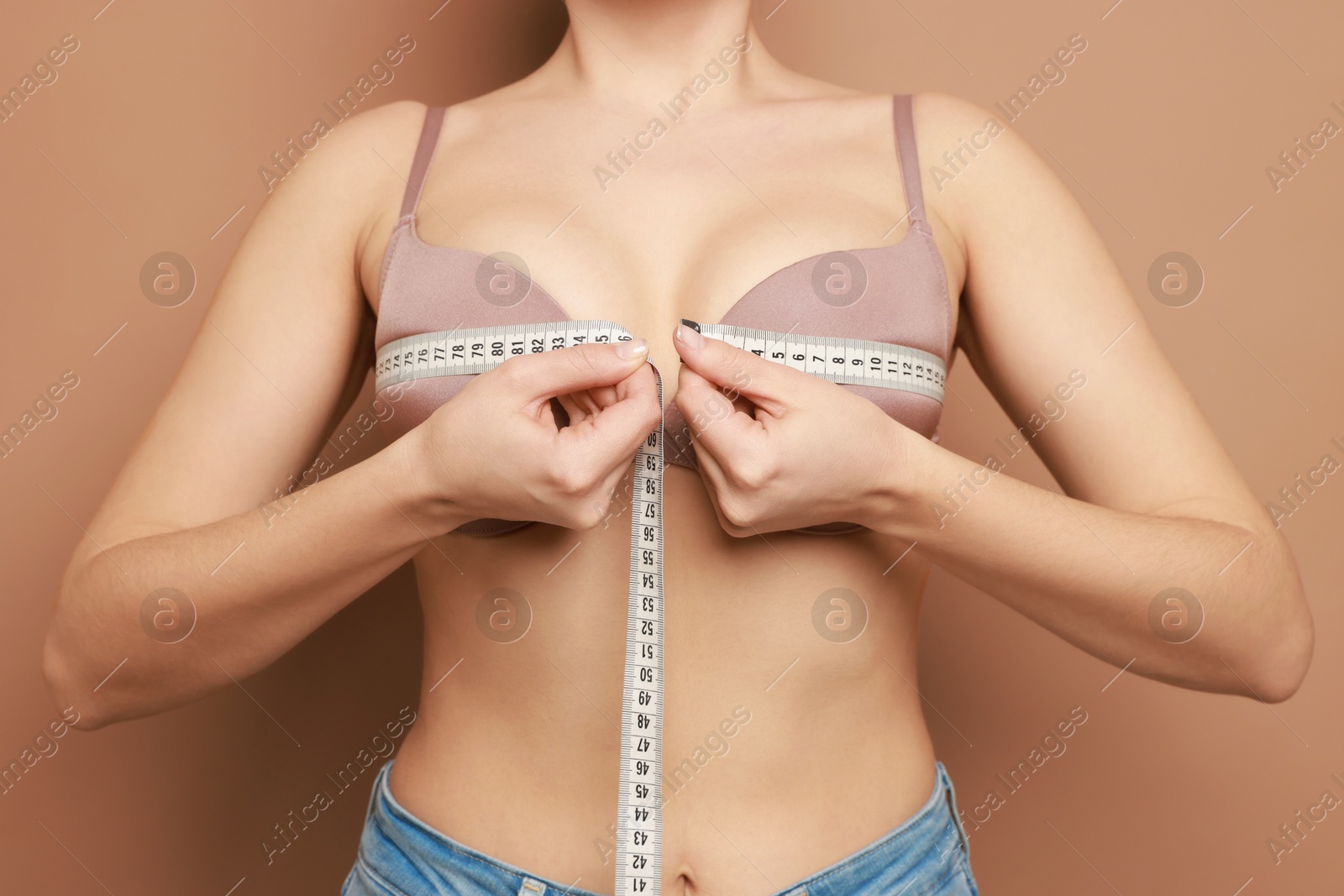 Photo of Woman in beautiful bra measuring breast circumference on beige background, closeup