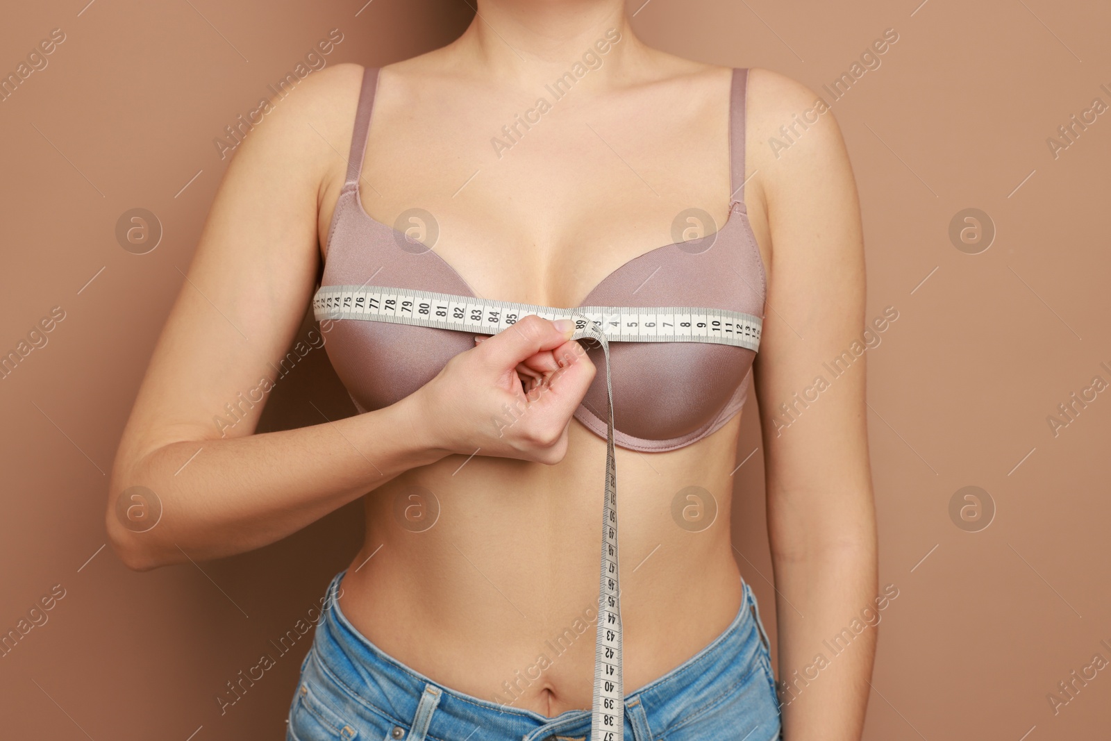 Photo of Woman in beautiful bra measuring breast circumference on beige background, closeup