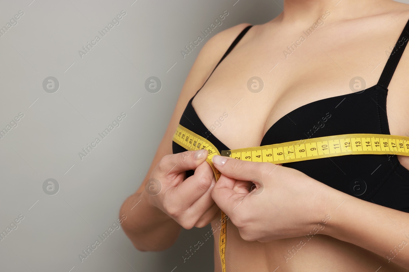 Photo of Woman in beautiful bra measuring breast circumference on light background, closeup. Space for text