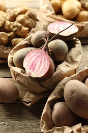 Photo of Different raw root vegetables in paper bags on wooden table, closeup