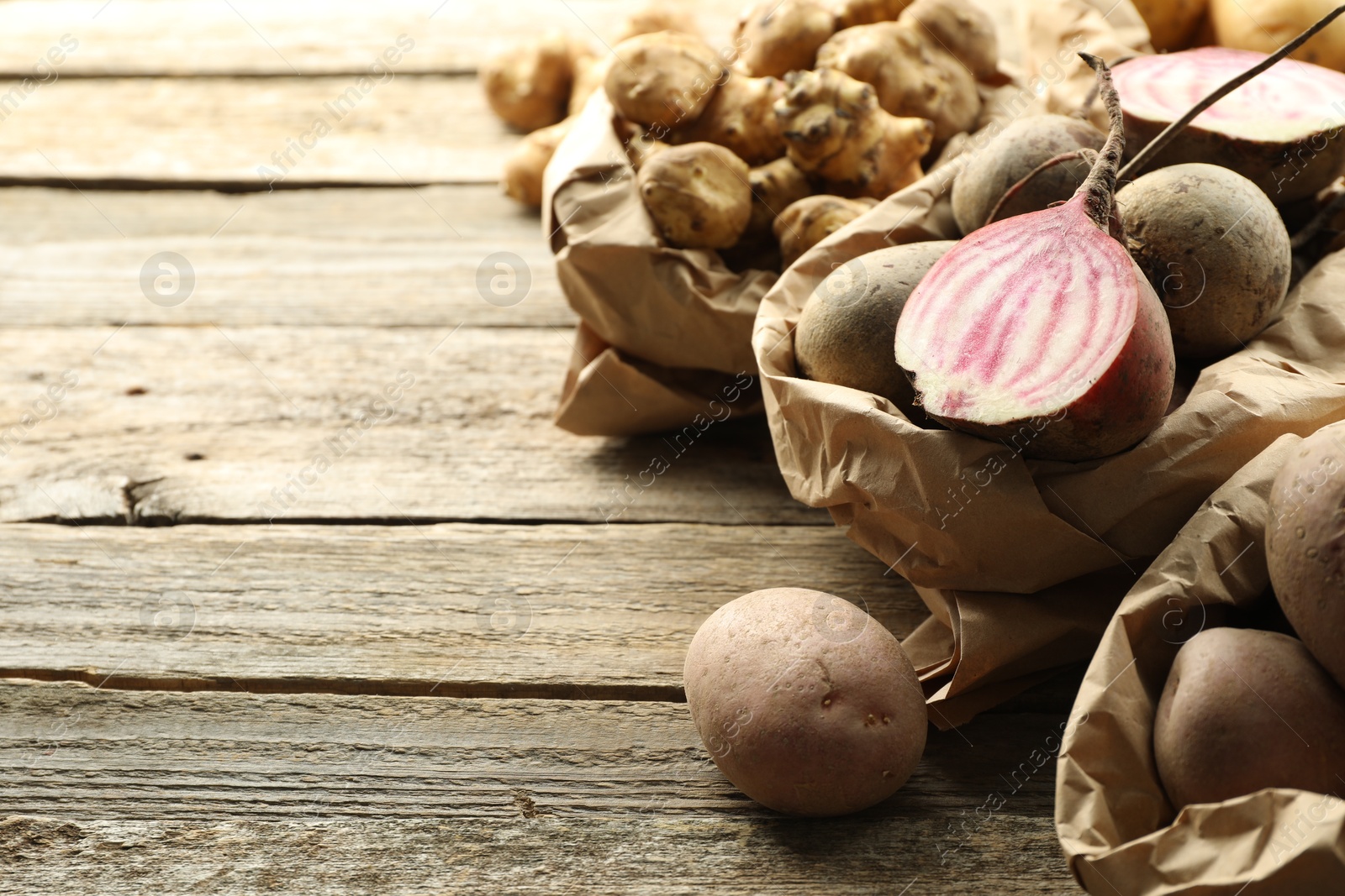 Photo of Different raw root vegetables in paper bags on wooden table, closeup. Space for text