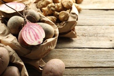 Photo of Different raw root vegetables in paper bags on wooden table, closeup. Space for text