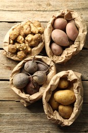 Photo of Different raw root vegetables in paper bags on wooden table, flat lay