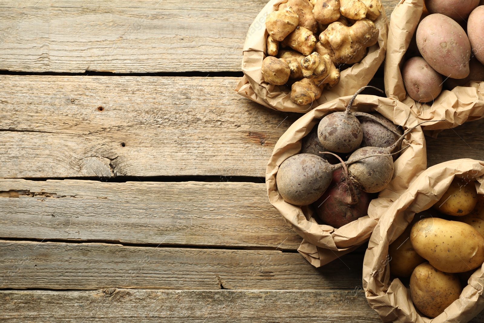 Photo of Different raw root vegetables in paper bags on wooden table, flat lay. Space for text