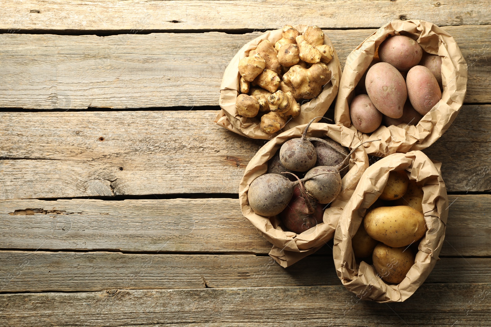 Photo of Different raw root vegetables in paper bags on wooden table, flat lay. Space for text