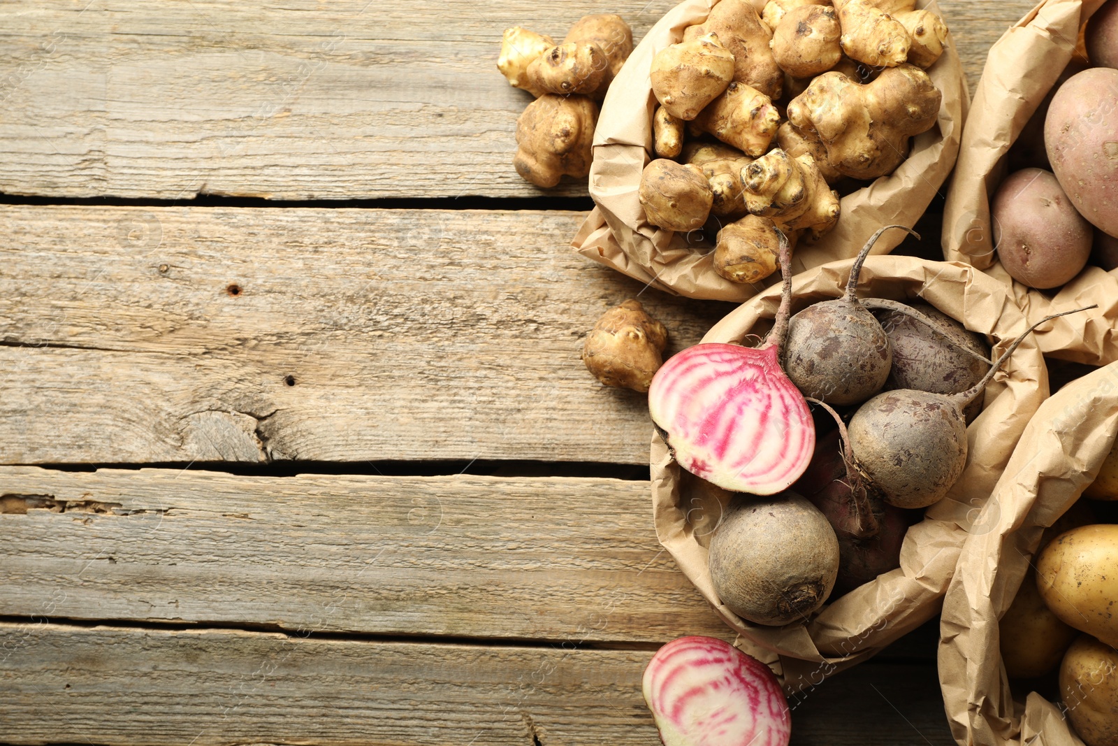 Photo of Different raw root vegetables in paper bags on wooden table, flat lay. Space for text