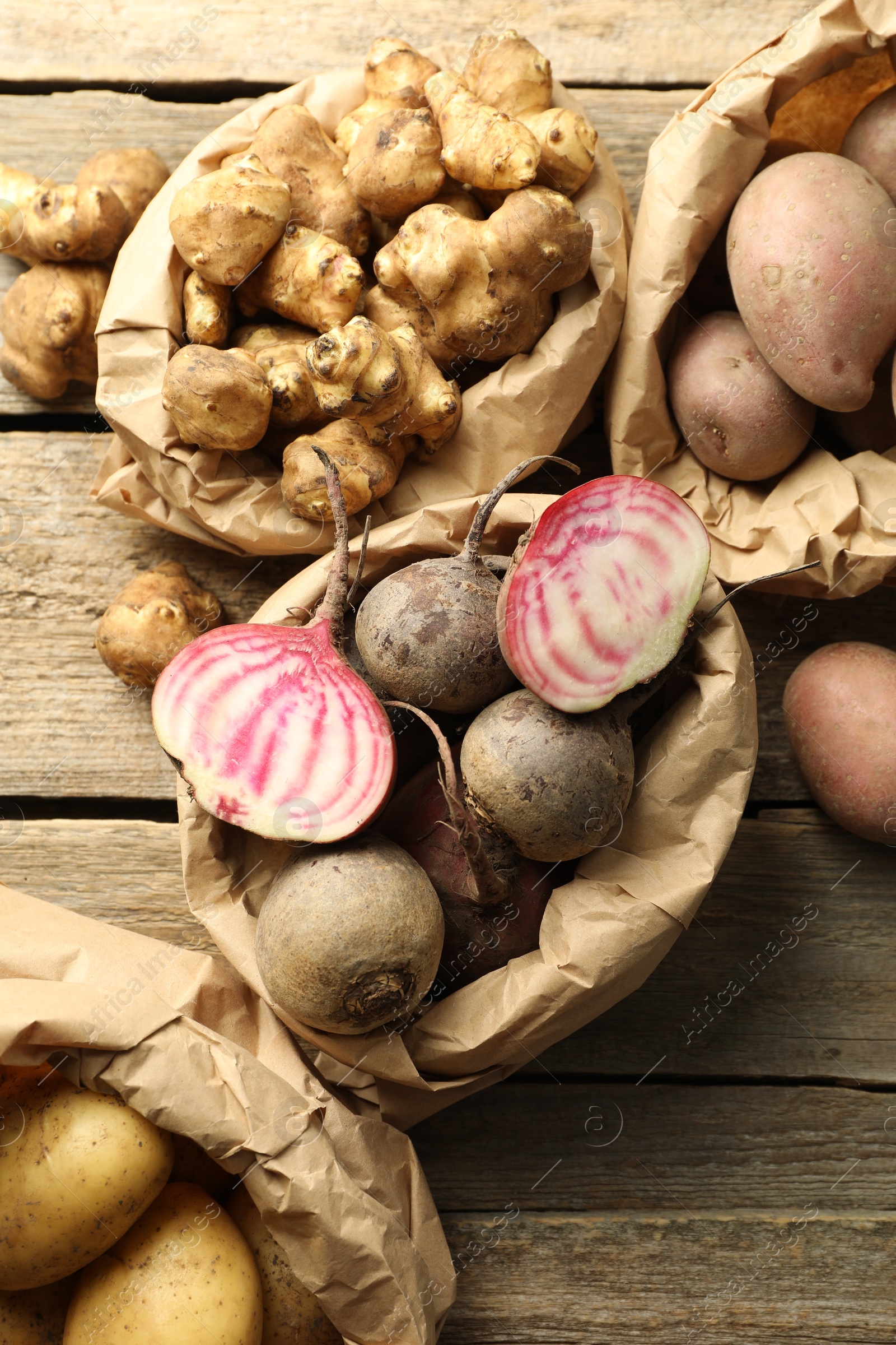 Photo of Different raw root vegetables in paper bags on wooden table, flat lay