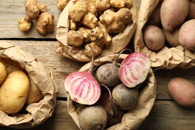 Photo of Different raw root vegetables in paper bags on wooden table, flat lay