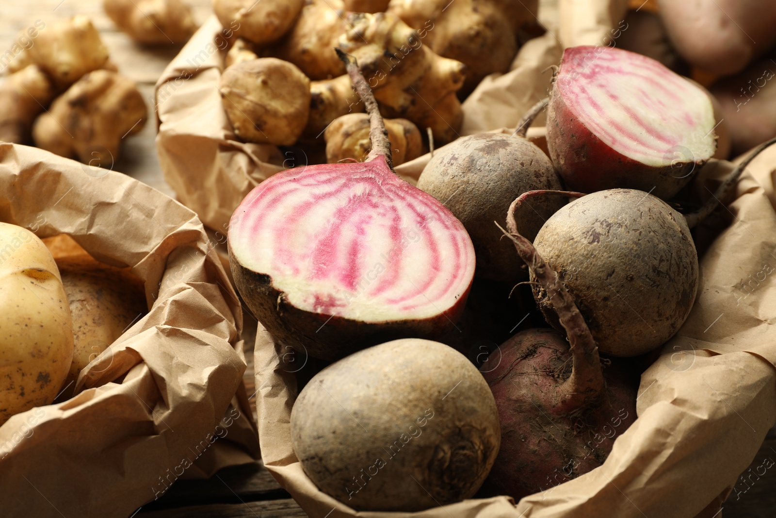 Photo of Different raw root vegetables in paper bags on table, closeup