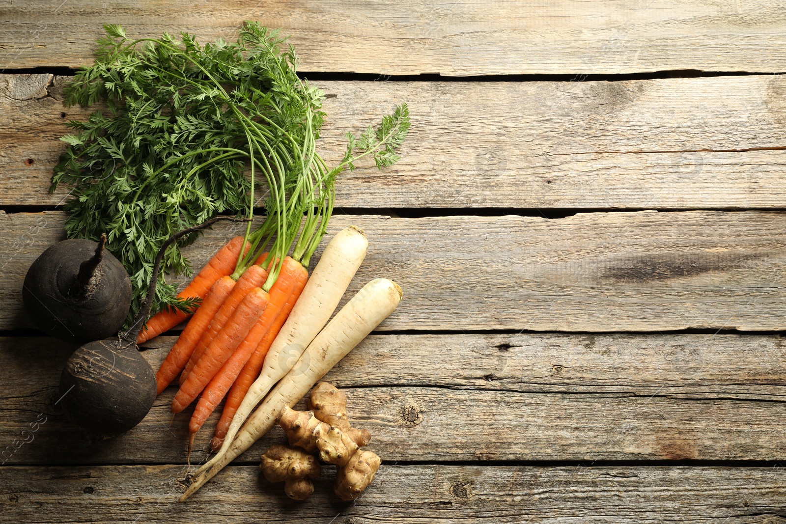 Photo of Different root vegetables on wooden table, flat lay. Space for text