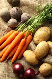 Photo of Different root vegetables on burlap fabric, flat lay