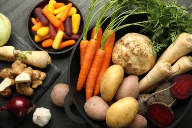 Photo of Different raw root vegetables on black table, flat lay