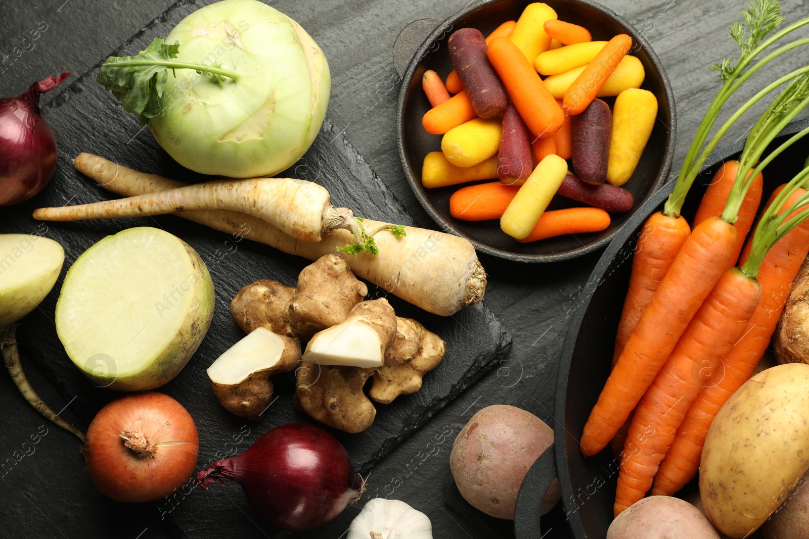 Photo of Different raw root vegetables on black table, flat lay