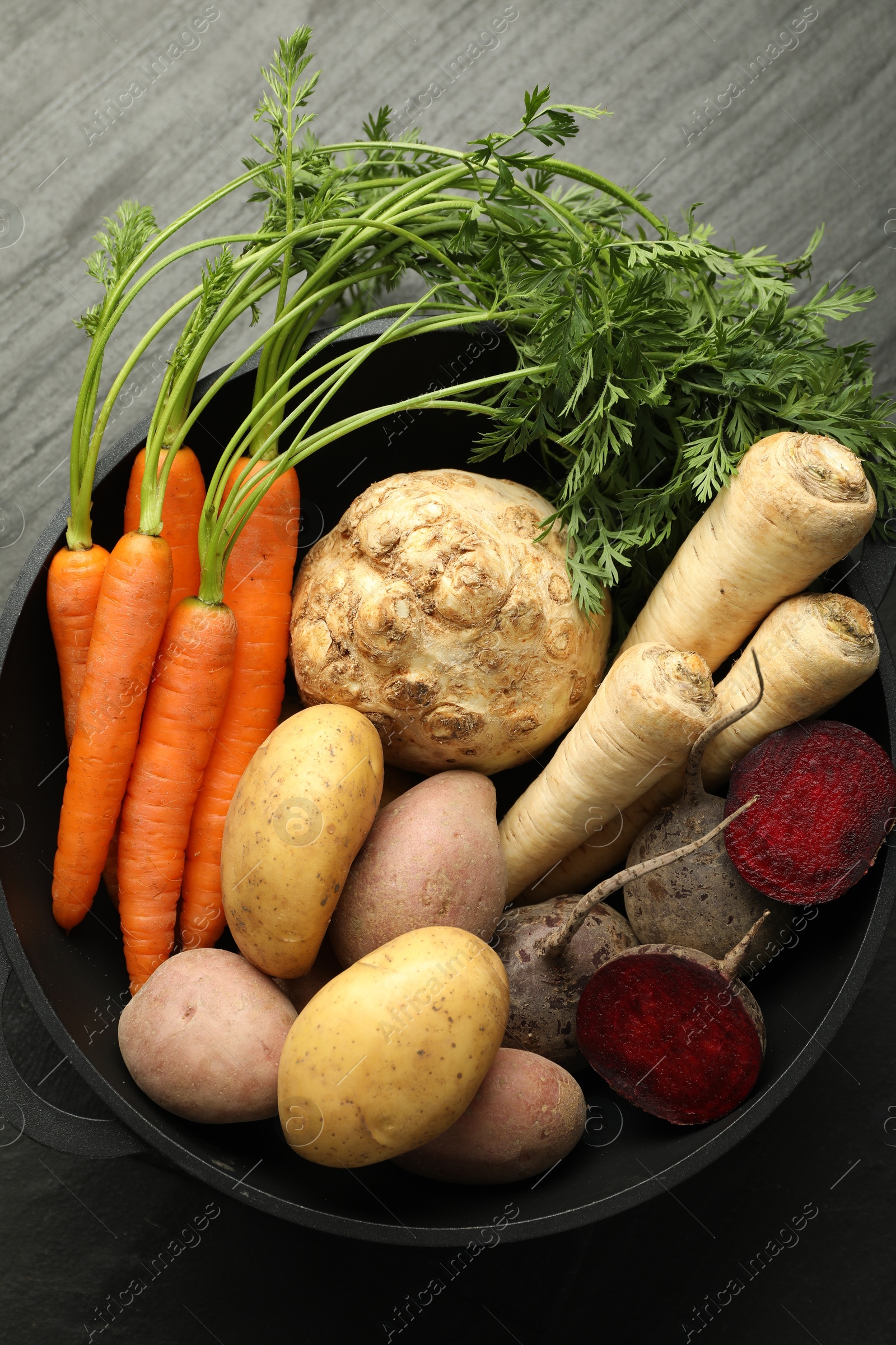 Photo of Different root vegetables in pot on black table, top view