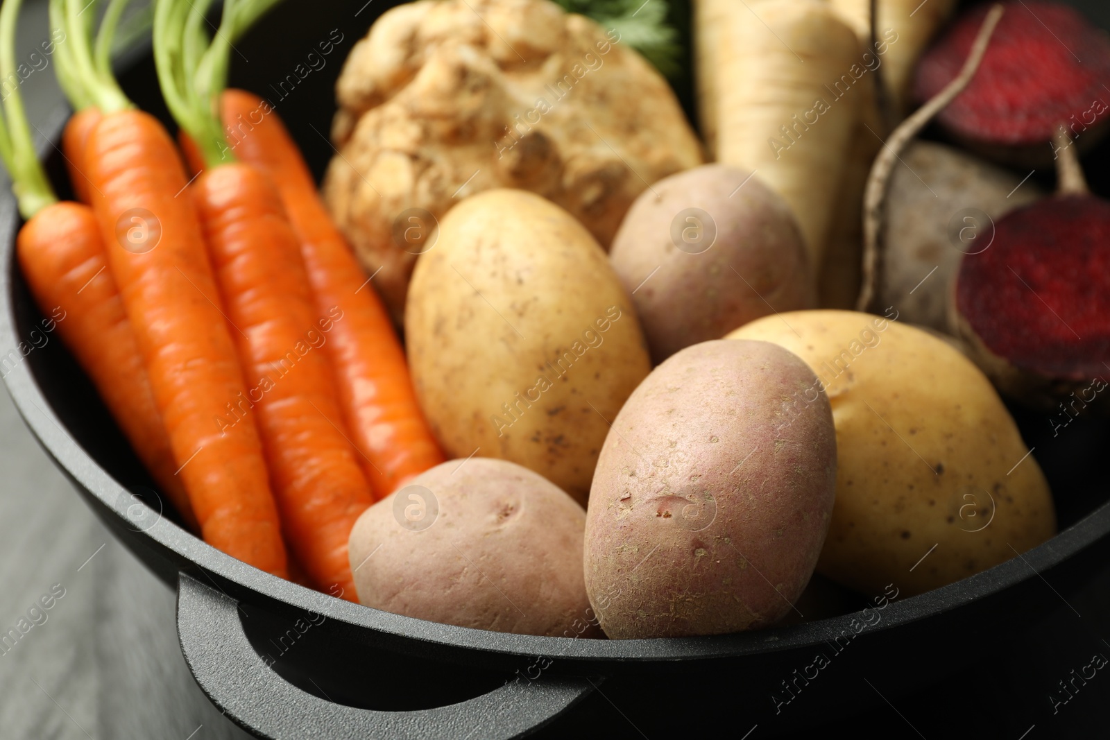 Photo of Different root vegetables in pot on black table, closeup