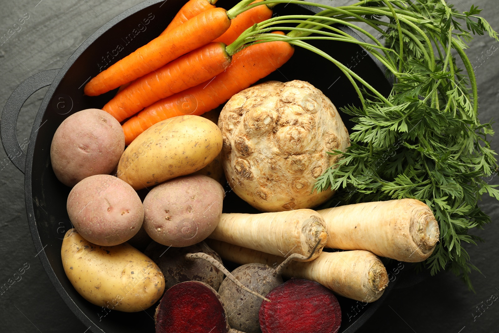 Photo of Different root vegetables in pot on black table, top view