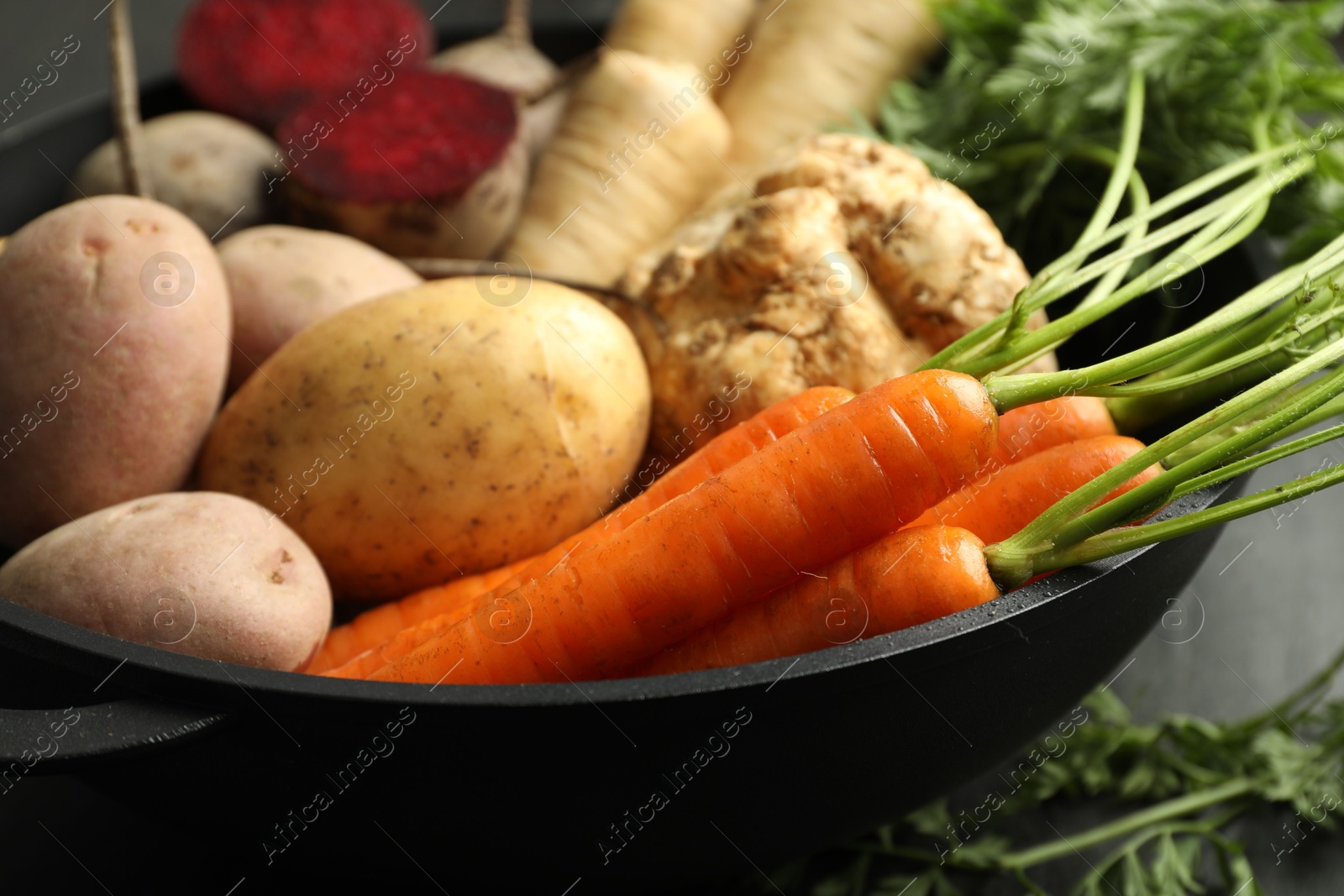 Photo of Different root vegetables in pot on black table, closeup