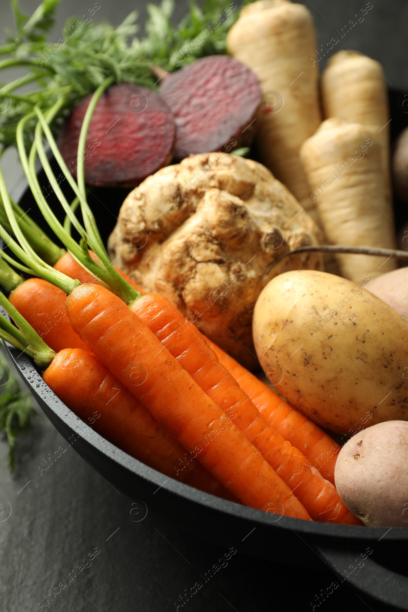 Photo of Different root vegetables in pot on black table, closeup