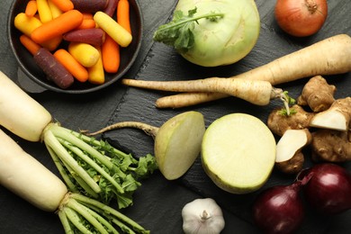 Photo of Different raw root vegetables on black table, flat lay