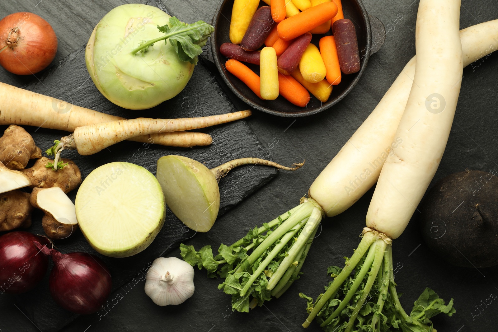 Photo of Different raw root vegetables on black table, flat lay