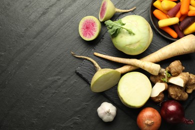 Photo of Different raw root vegetables on black table, flat lay. Space for text