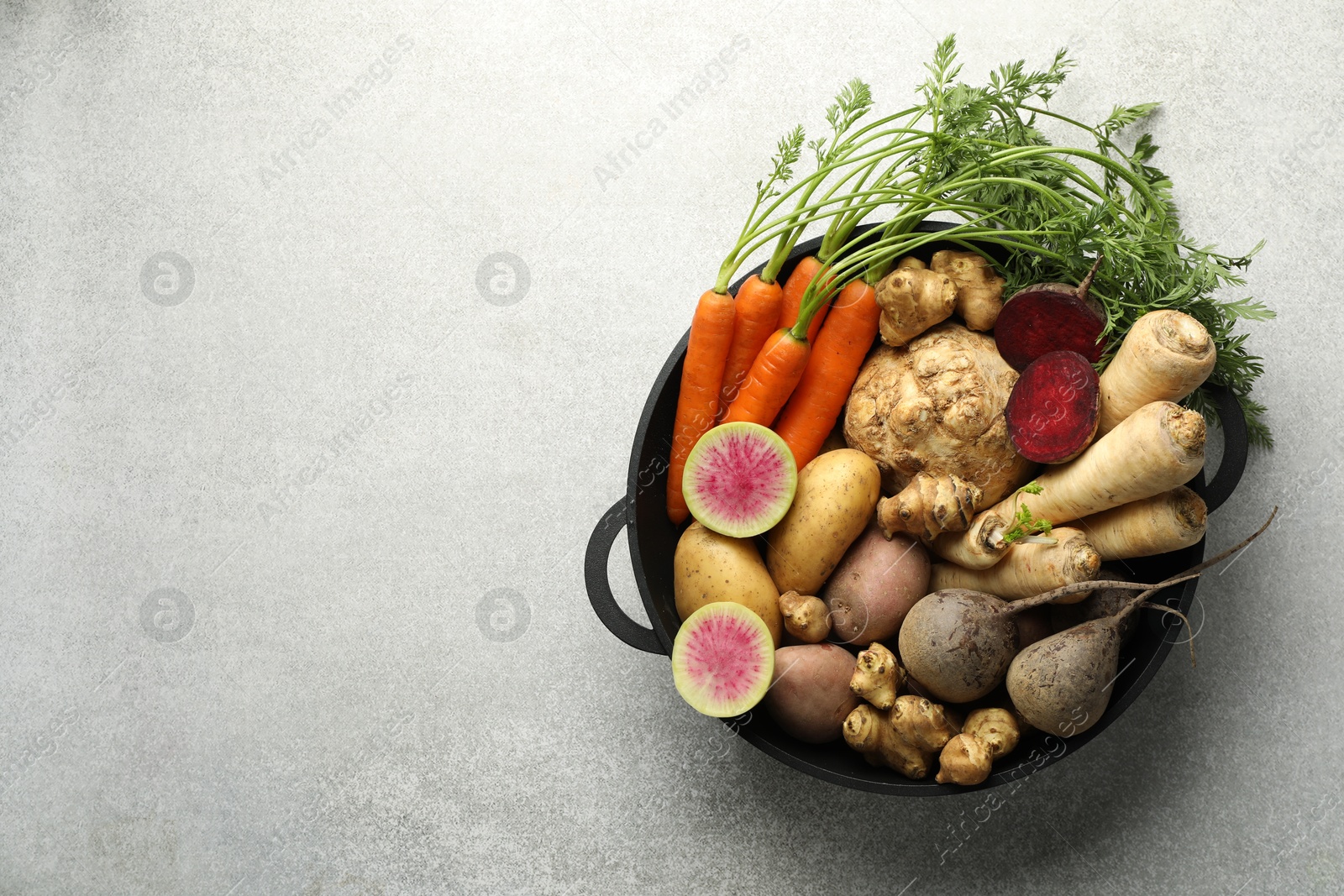 Photo of Different root vegetables in pot on light grey table, top view. Space for text