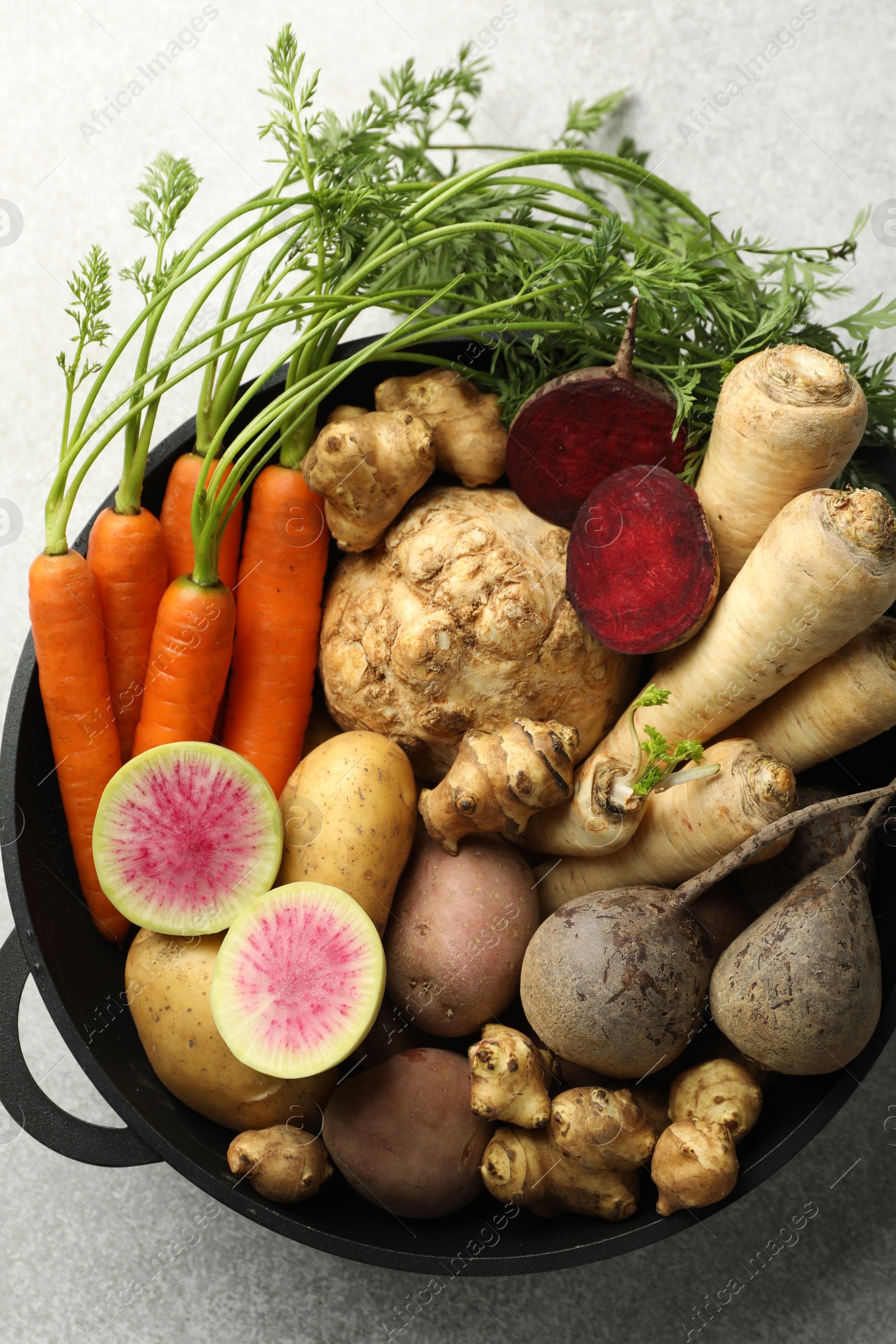 Photo of Different root vegetables in pot on light grey table, top view